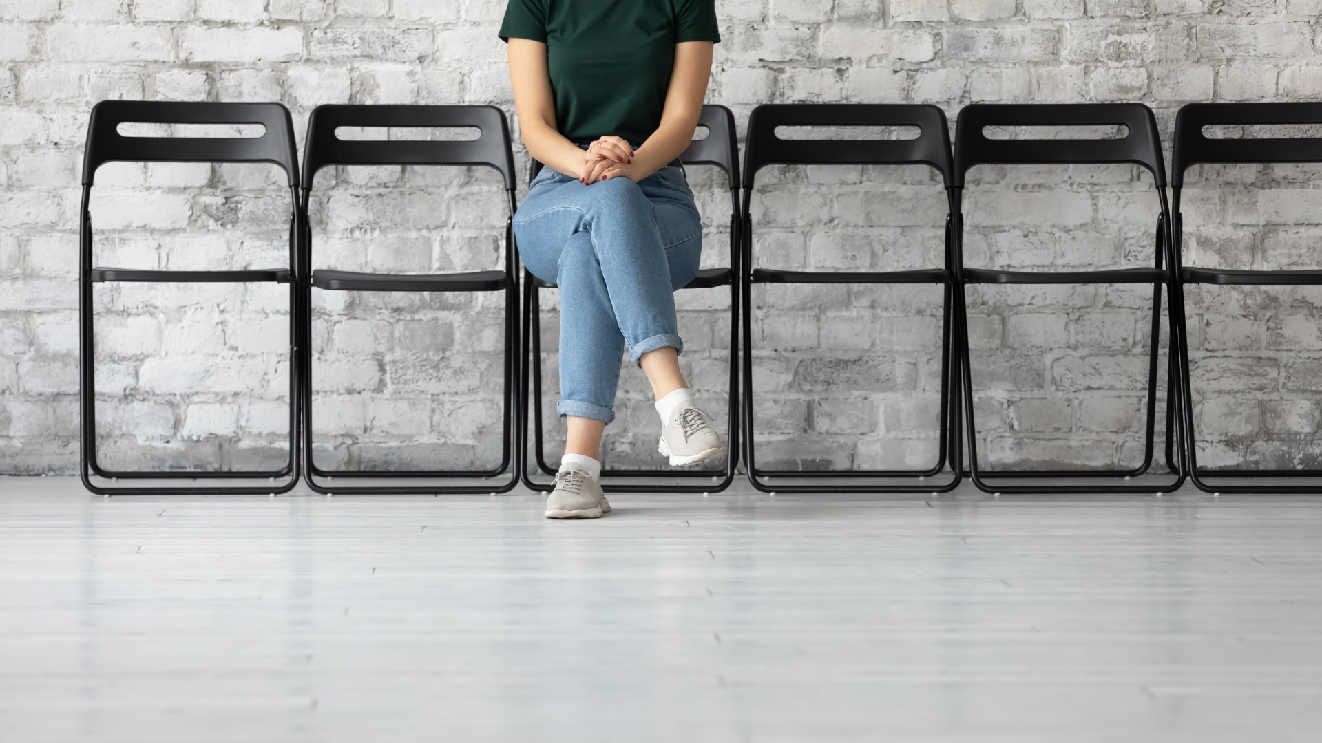 A person sits on a chair located in a row of chairs in front of a brick wall